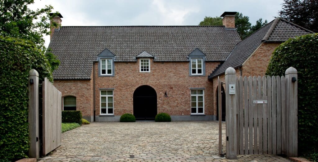 Charmante maison en briques rouges avec un toit en tuiles traditionnelles, équipée de châssis bois Profel. L’entrée, encadrée par une allée pavée et un portail en bois, renforce le caractère rustique et accueillant de la propriété. Les fenêtres en châssis bois Profel offrent à la fois une isolation performante et une esthétique intemporelle qui s’harmonise parfaitement avec l’architecture classique de la maison.