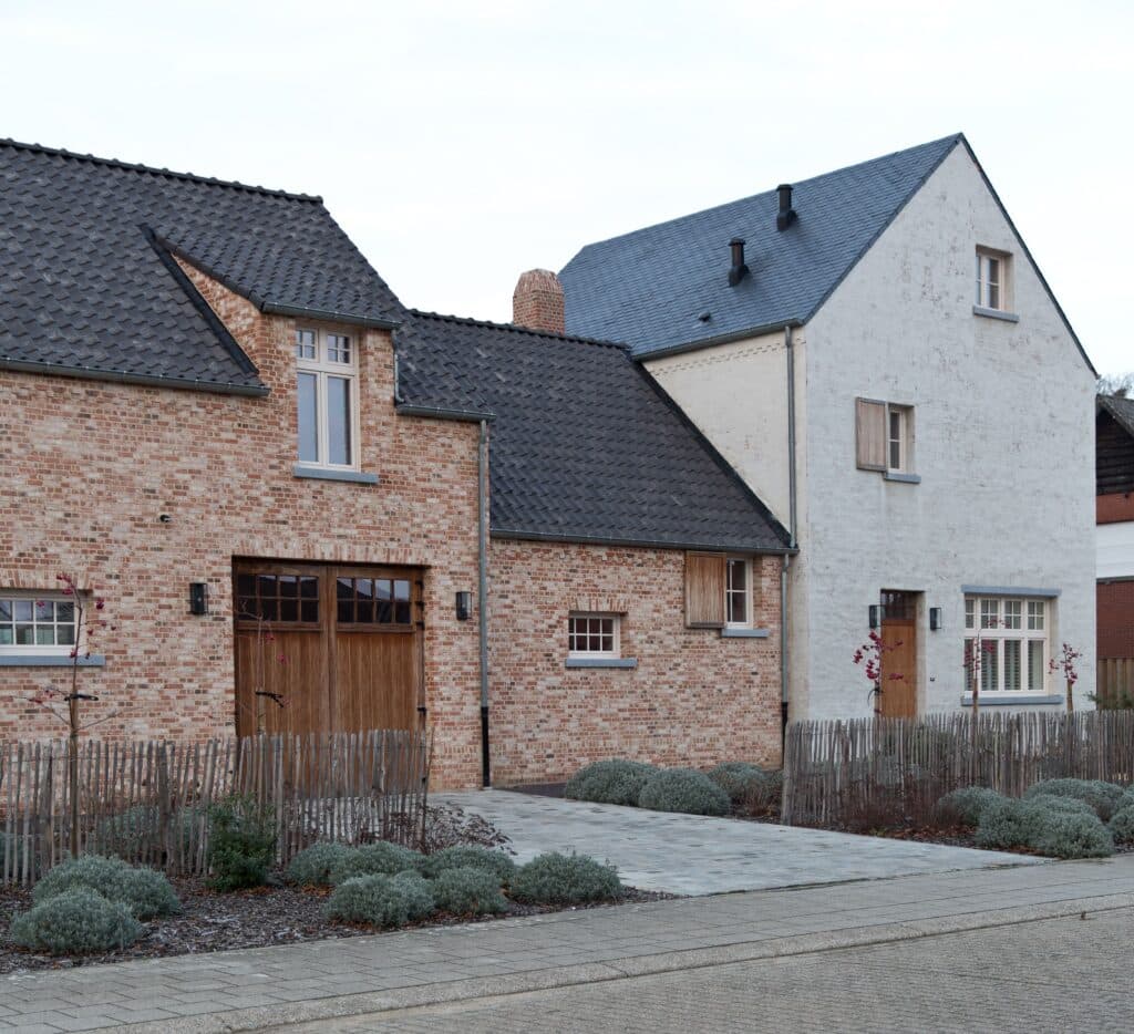 Deux maisons de style traditionnel avec des façades en briques rouges et blanches, équipées de châssis bois Profel. Les toits en tuiles et les portes en bois complètent le charme rustique et authentique de ces habitations. Les fenêtres en châssis bois Profel apportent une touche moderne tout en respectant l'esthétique classique des bâtiments.