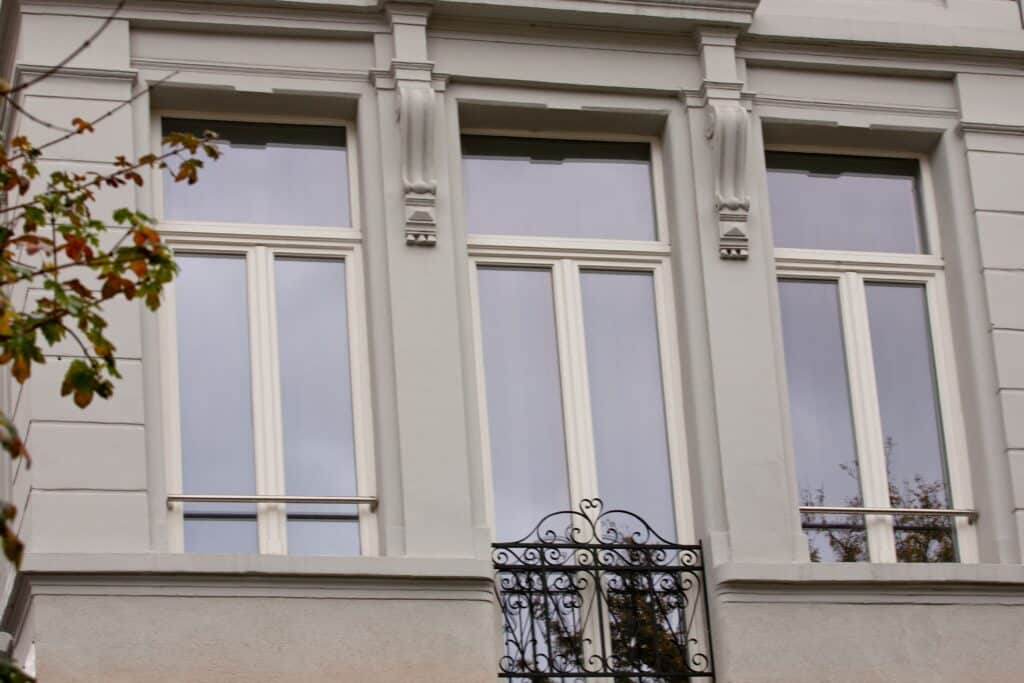 Façade élégante d’un bâtiment classique avec des châssis bois Profel, parfaitement intégrés dans une architecture aux détails ornementaux raffinés. Les fenêtres, aux cadres en bois blanc, apportent une luminosité naturelle tout en conservant le cachet traditionnel de l'immeuble. La ferronnerie décorative sous les fenêtres ajoute une touche de distinction à l'ensemble