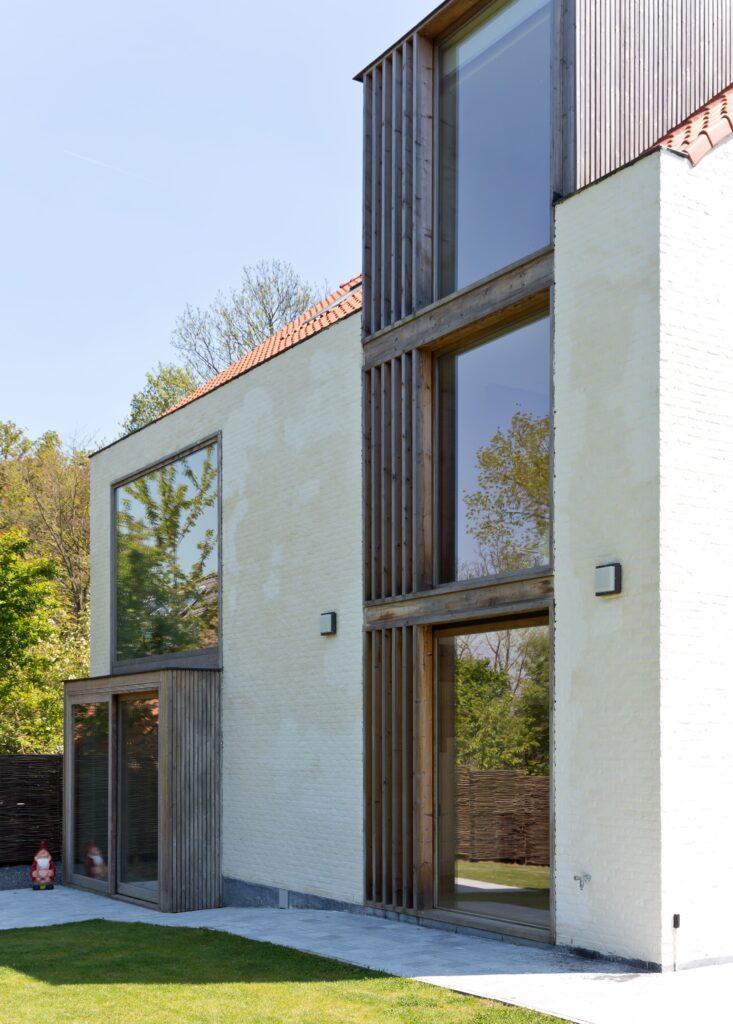 Maison moderne avec une façade épurée, équipée de grandes baies vitrées en châssis bois Profel. Les lignes verticales des fenêtres et le cadre en bois accentuent l’architecture contemporaine de la maison, tout en offrant une ouverture maximale sur l'extérieur. Les châssis bois Profel garantissent une isolation thermique optimale, tout en s'intégrant parfaitement au design moderne et minimaliste de cette propriété.